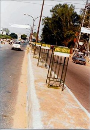 A row of ‘Harit Dilli’ (Green Delhi) branded tree guards on a road median — empty. The saplings they were installed to protect are gone. The guards, and the programme’s name, remain